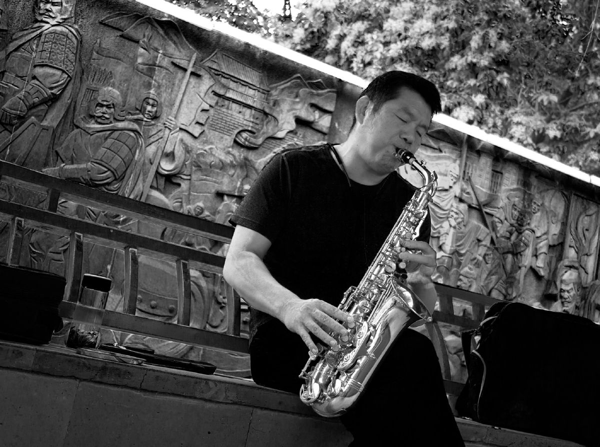 A saxophonist plays before an ancient warrior relief, bridging modern melody with historical echoes.