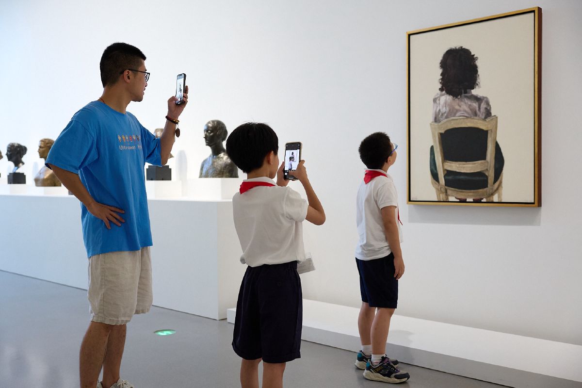 Young students photograph portraits in a gallery, capturing art through their own curious lenses.
