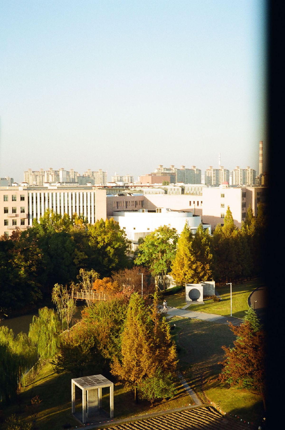 Autumn sunlight bathes a university campus in warm golden hues, with trees displaying fall colors between modern buildings.