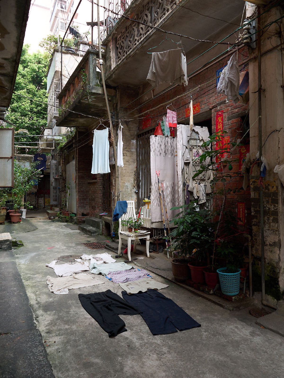Laundry hangs from weathered balconies above a narrow alleyway where clothes dry on the sun-warmed concrete below.