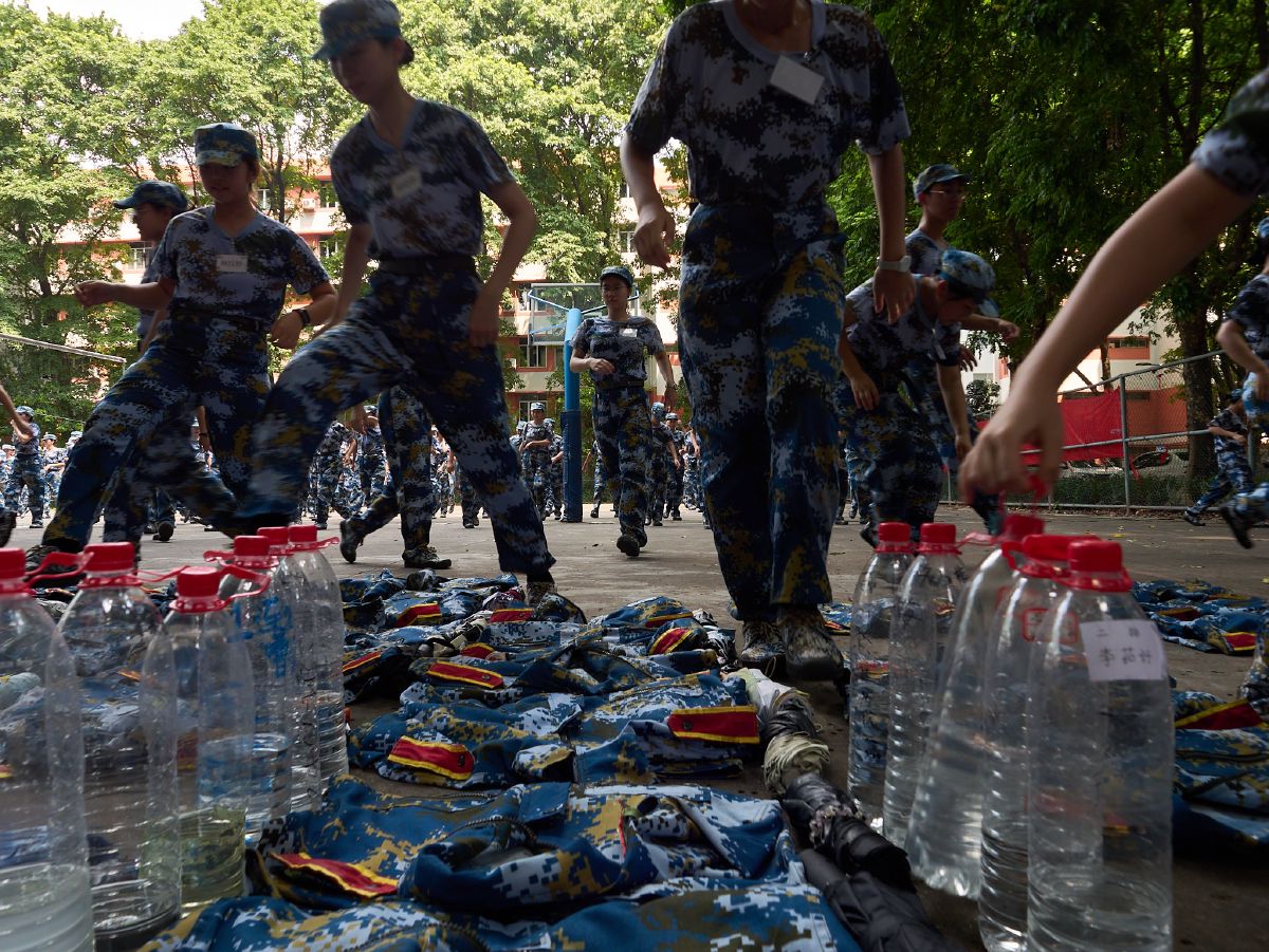 Students in camouflage uniforms march past water bottles and discarded jackets during a break in their military training exercises.