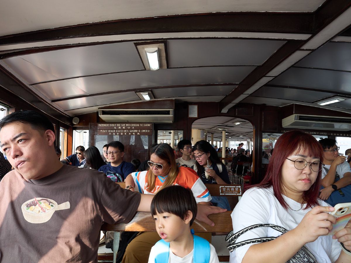 Passengers ride the historic Star Ferry across Victoria Harbour, seated on wooden benches inside the classic vessel's interior.