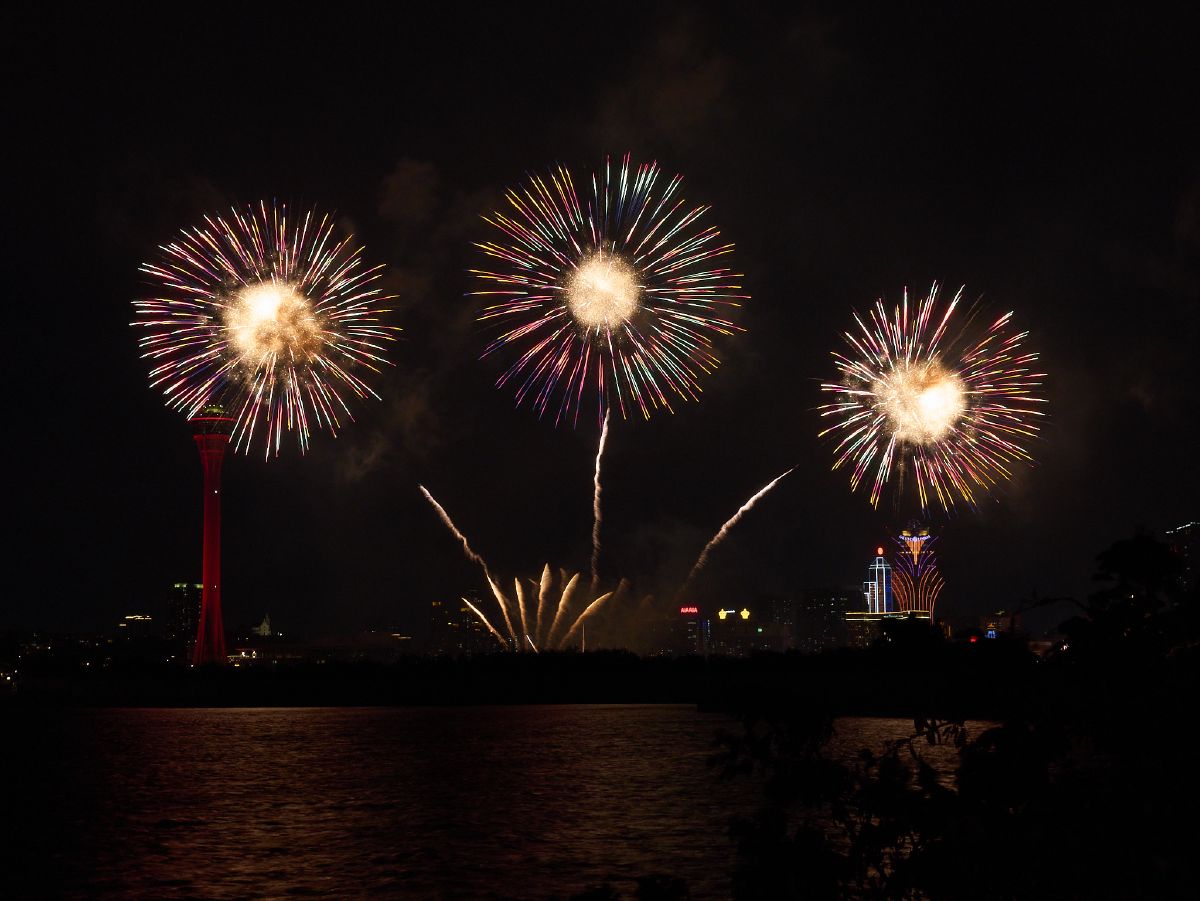 Brilliant fireworks explode above the Macau Tower and Grand Lisboa, reflecting off the dark waters of the harbor during the National Day celebration.