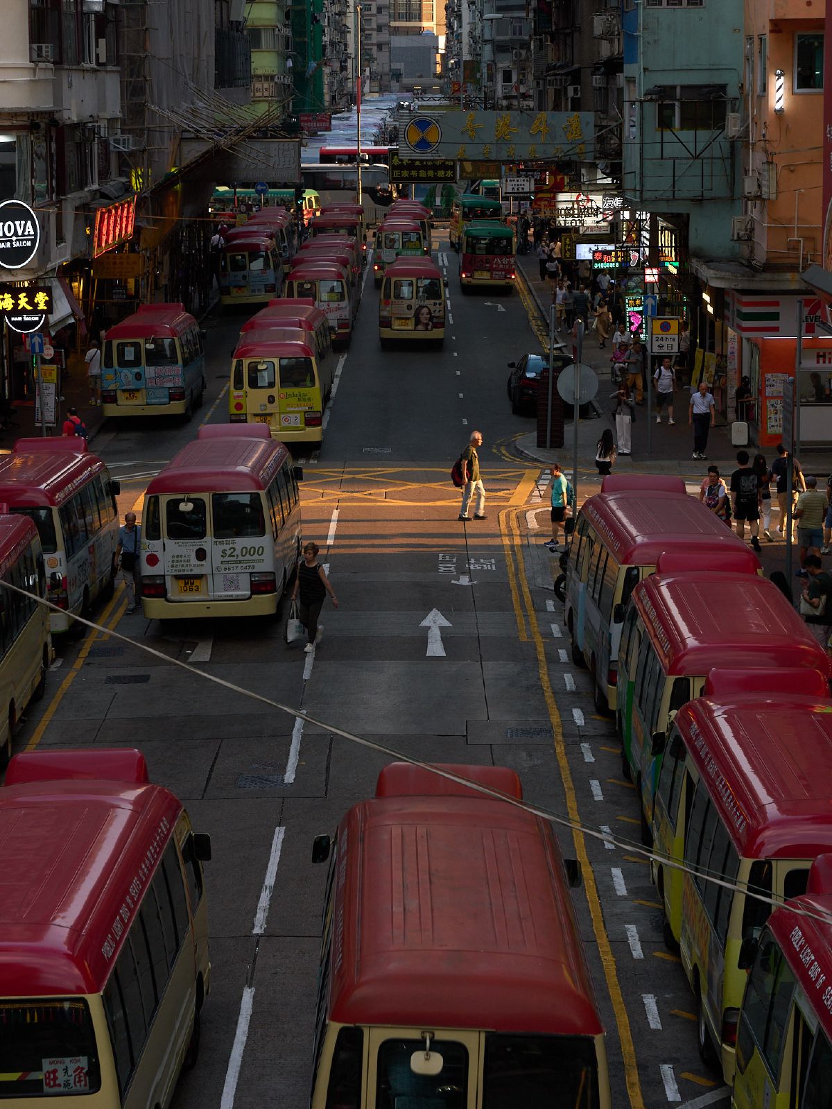 Rows of red-roofed minibuses line both sides of a bustling Mong Kok street as pedestrians navigate the crosswalk below.