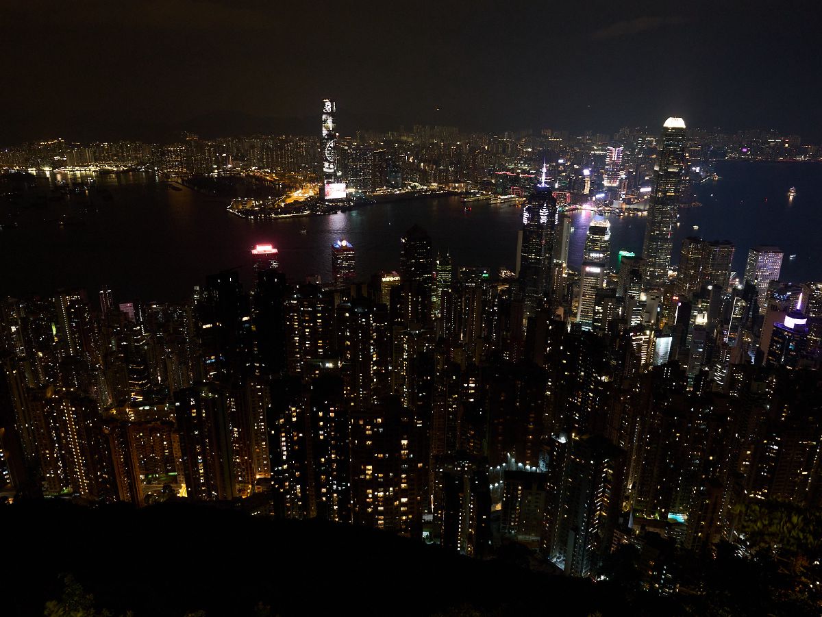 A panoramic nighttime view captures the dazzling lights of Central and Kowloon separated by the dark waters of Victoria Harbour.