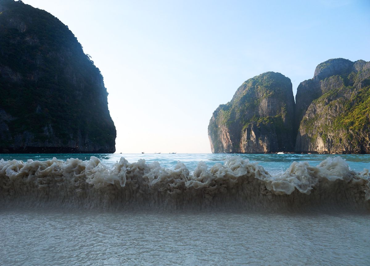Foamy waves break on the shore between two majestic limestone cliffs rising from Krabi's crystal-clear turquoise sea.