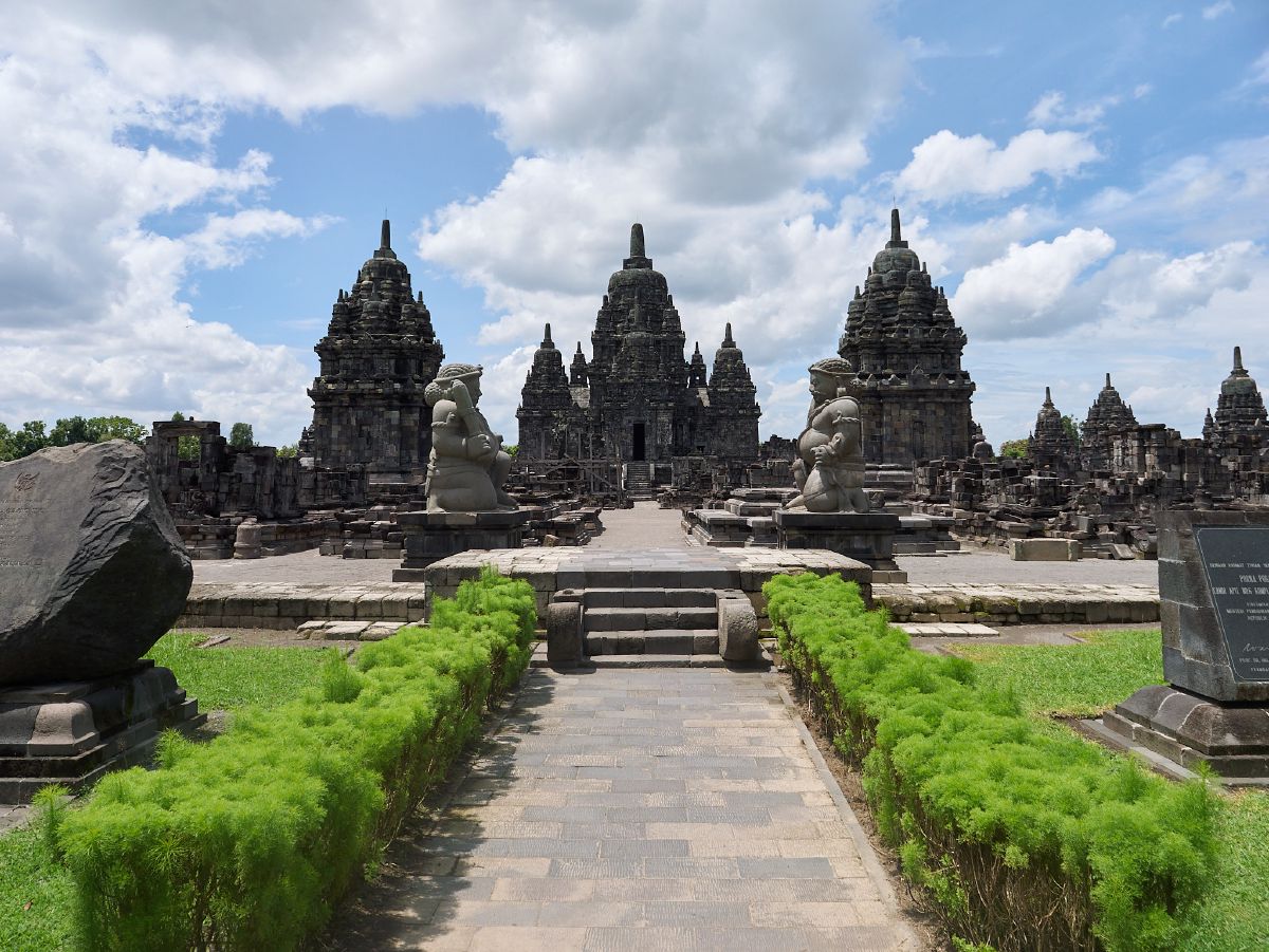 A grand pathway lined with guardian statues leads to towering spires of Yogyakarta's majestic Prambanan temple.