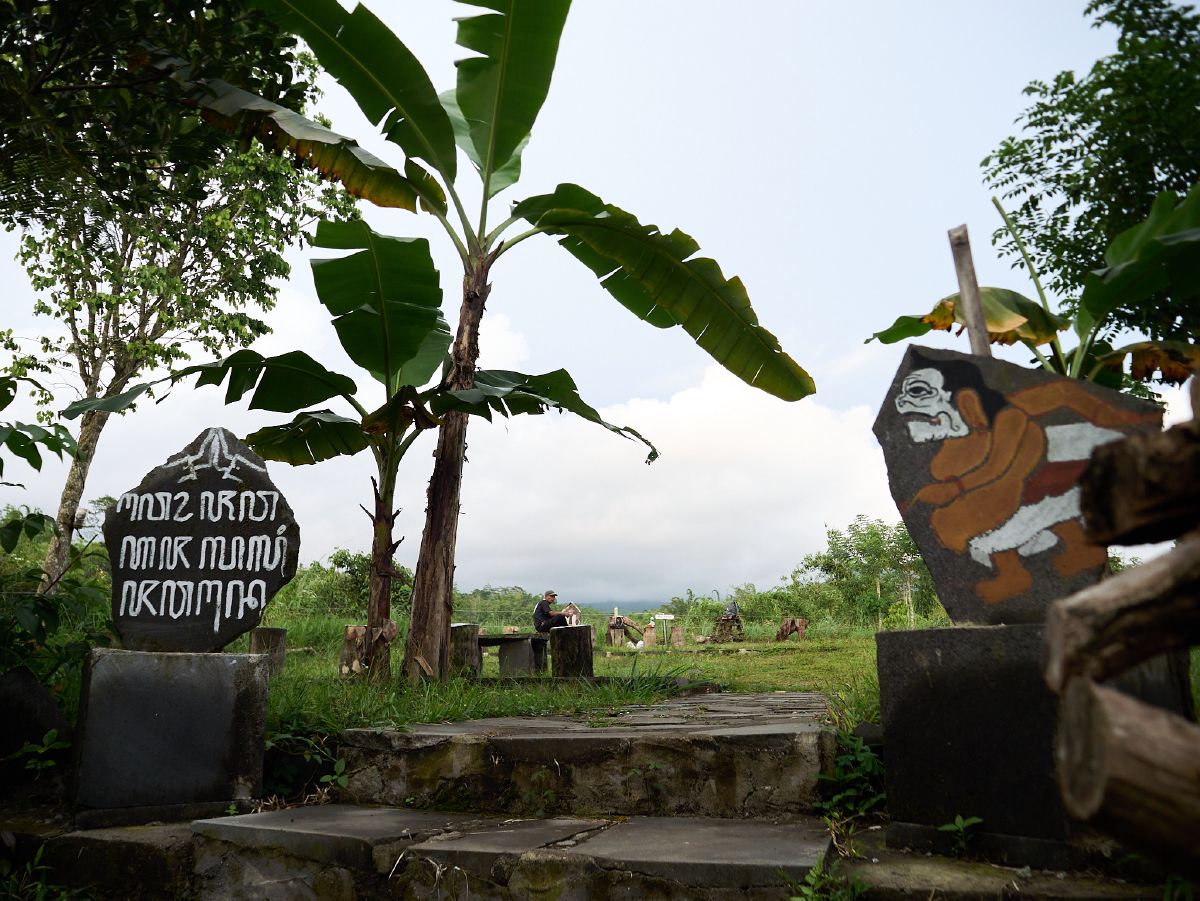 Painted stone markers carved with ancient Javanese script frame a rustic path through Yogyakarta's rural countryside.