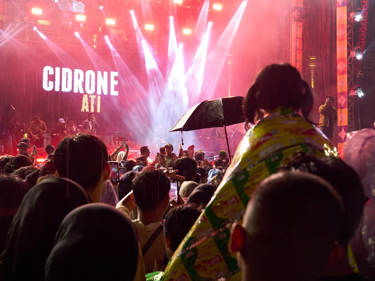 A crowd gathers under red stage lights to watch the Cidrone Ati band perform during a rainy New Year's concert in Malang.