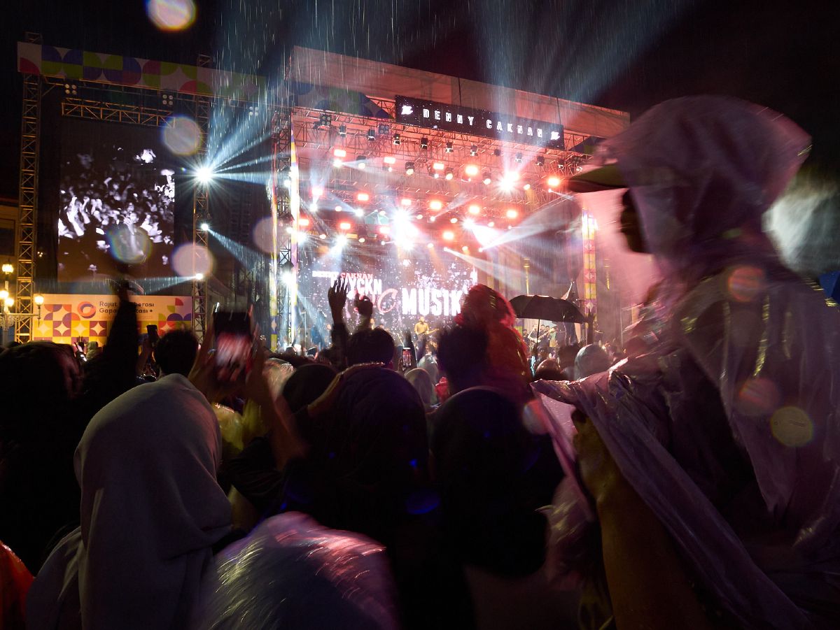 Concertgoers brave the rain to watch performers on a brightly lit stage during a New Year's music festival in Malang.