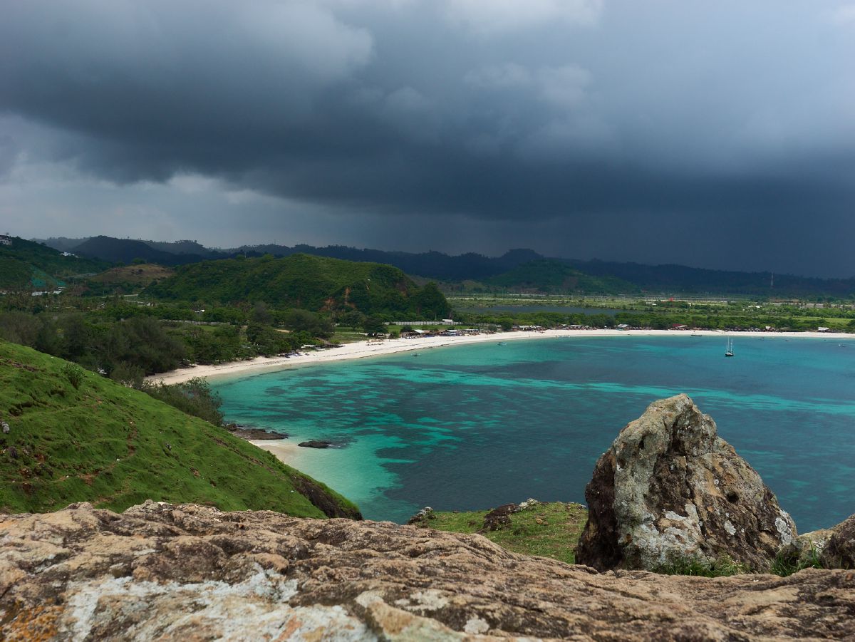 Dramatic storm clouds gathering over a pristine white sand beach with crystal-clear turquoise waters in Lombok.