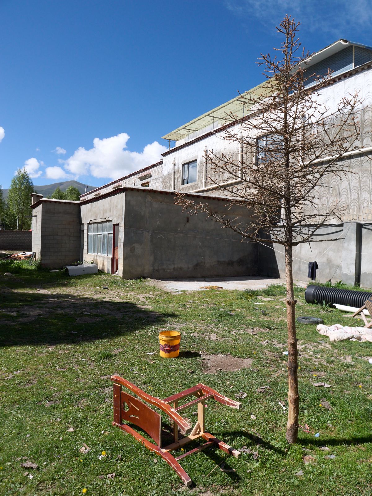 A traditional Tibetan house courtyard with a small bare tree and scattered household items under bright blue skies near Lhasa.