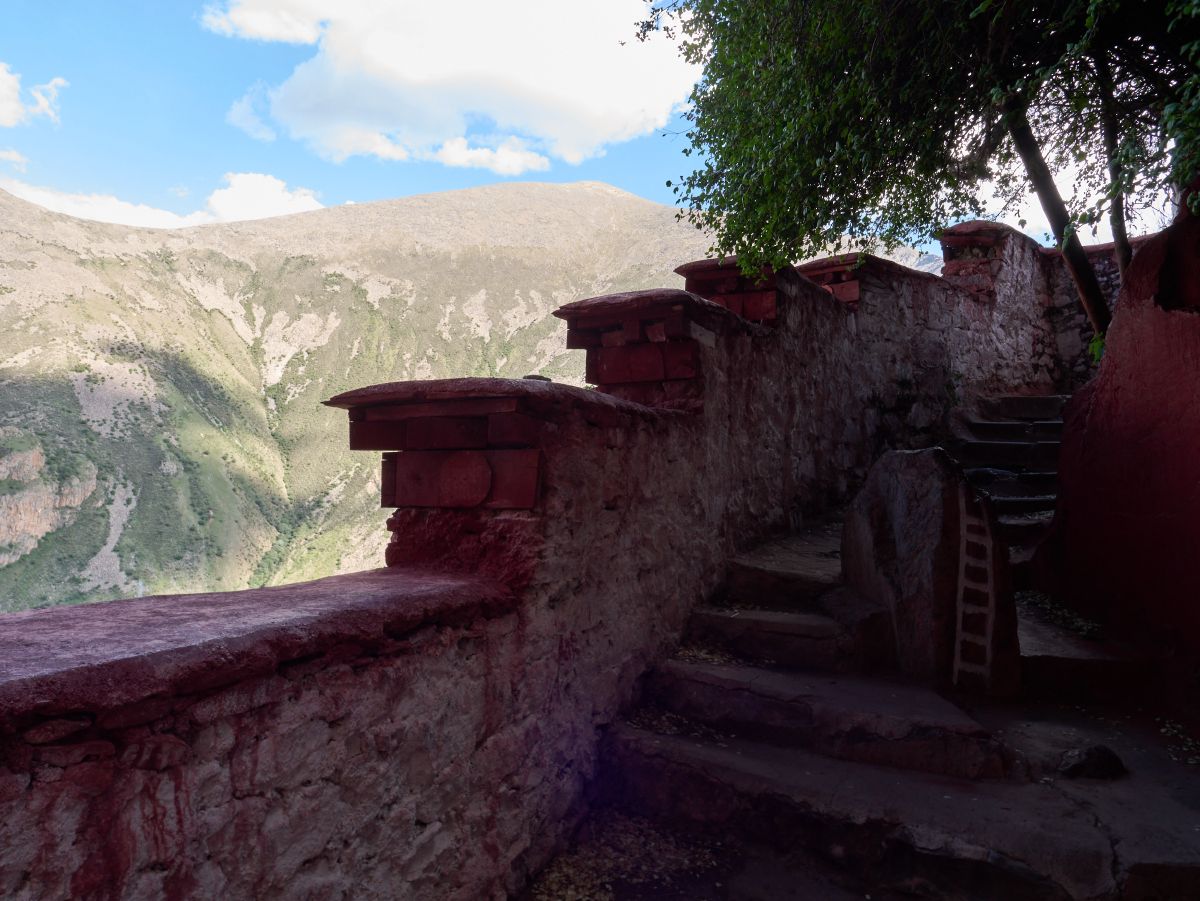 Weathered stone steps ascend alongside a traditional red-painted wall with the lush green valley and mountains visible in the background near Lhasa.